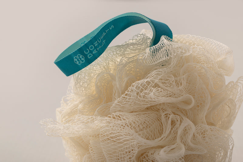 A close-up of a cream-colored loofah sponge with a teal blue hanging loop printed with the brand name Daily Concepts