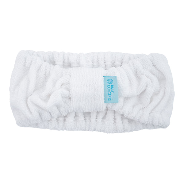 A white plush terry cloth headband with a central textured band and a small light blue fabric tag that reads 'DAILY CONCEPTS'.